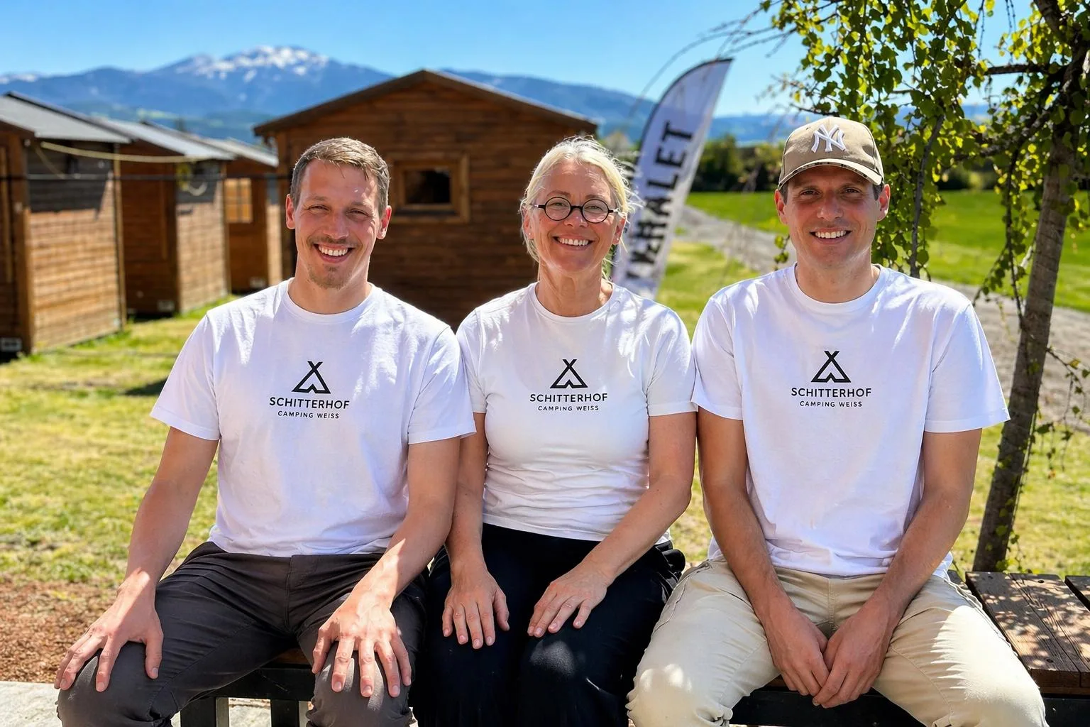 Lächelnde Gastgeber begrüßen Campinggäste am Schitterhof vor sonniger Wiesenkulisse