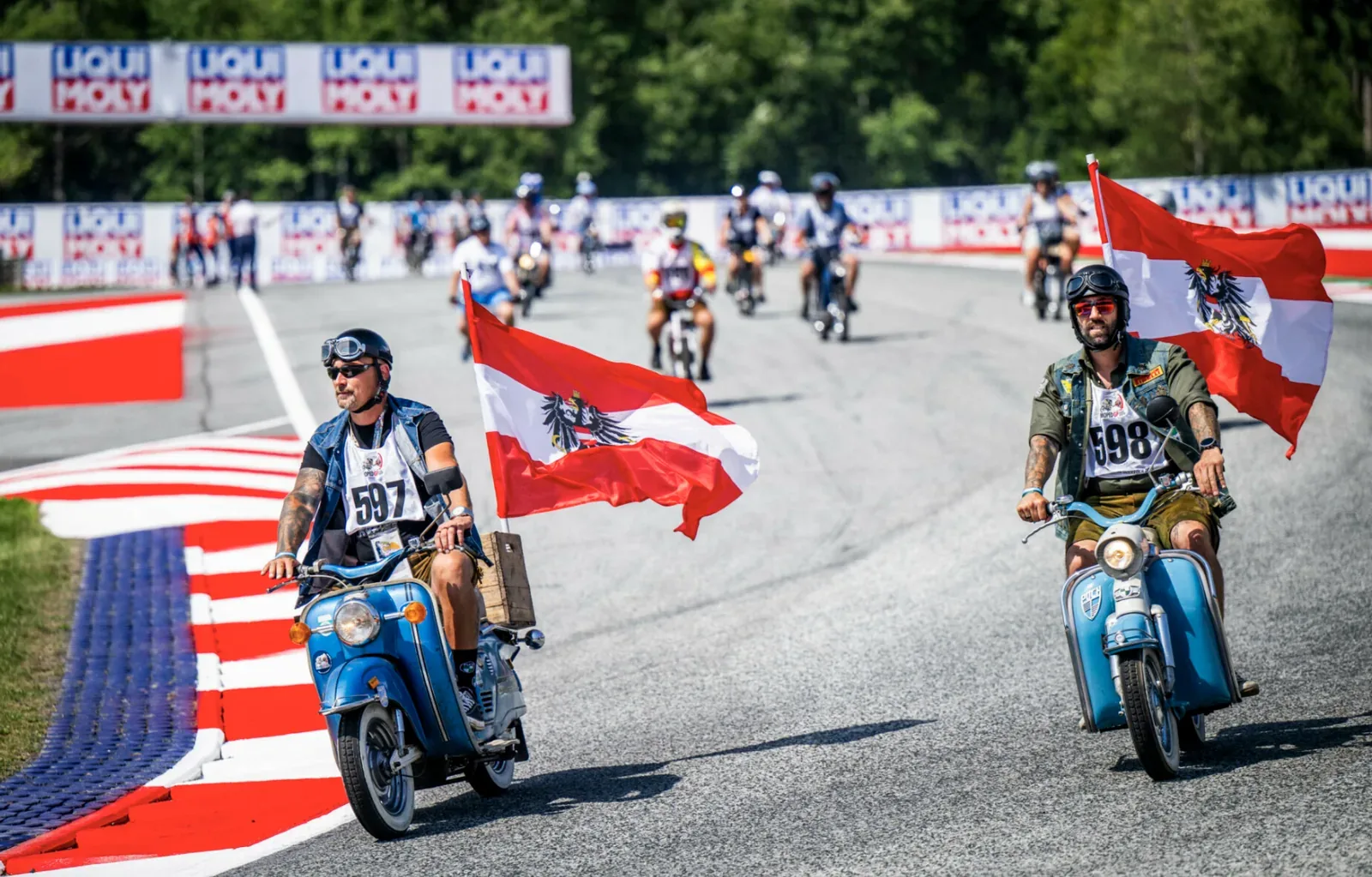 Zwei MopedGP-Fahrer mit Österreich-Fahnen auf der Rennstrecke des Red Bull Ring